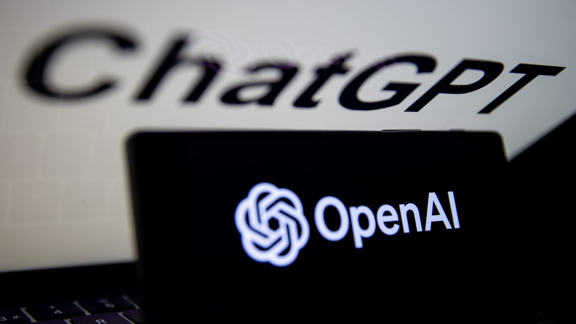 Le logo d'OpenAI est affiché sur l'écran d'un téléphone portable devant l'écran d'un ordinateur avec le logo de ChatGPT.