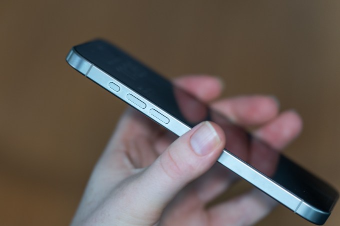 iPhone 15 Pro Max en titane naturel, tenu, montrant le côté du téléphone, y compris les boutons d'action et de volume.